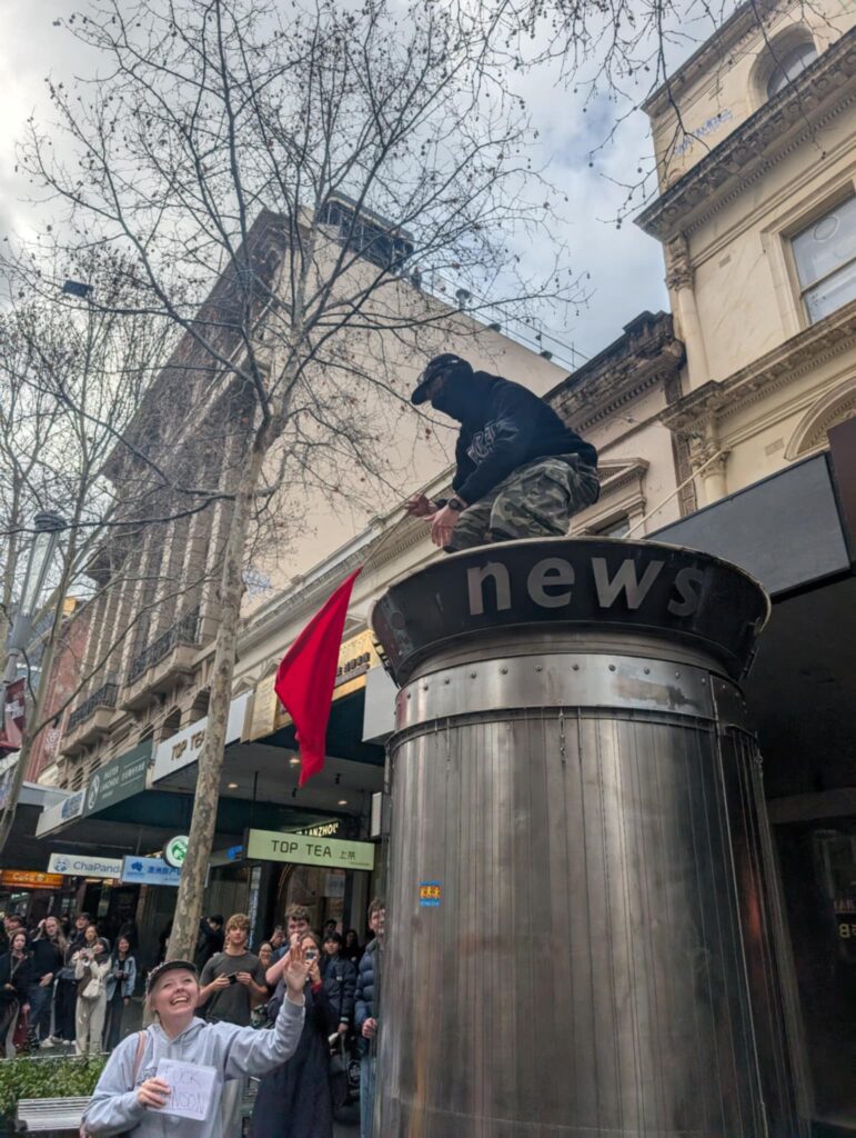 Onlookers cheer on a Communist supporter after climbing a news stand and waving his red flag. Picture: Josh Spasaro.